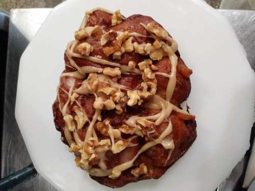 A delicious pastry topped with chopped walnuts and drizzled with a creamy glaze on a white plate.