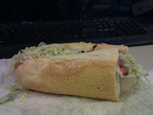 A large sandwich filled with lettuce and various meats, resting on a green patterned wrapper near a computer keyboard.
