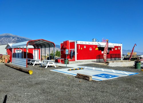 A bright red food stand with outdoor seating and a mountain backdrop under a clear blue sky.