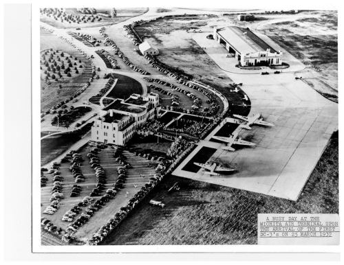 Aerial view of a busy airport terminal with cars and crowds, featuring several planes on the tarmac, dated March 25, 1957.