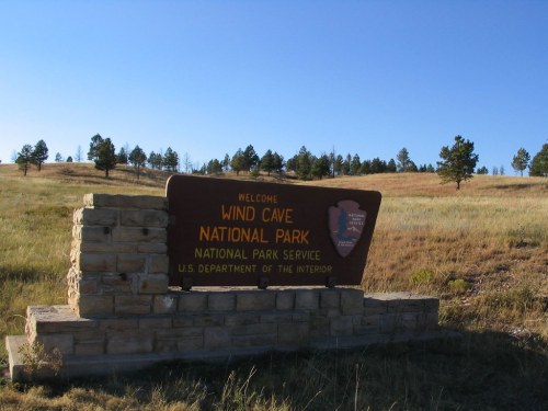 Welcome sign for Wind Cave National Park, surrounded by grassy fields and pine trees under a clear blue sky.