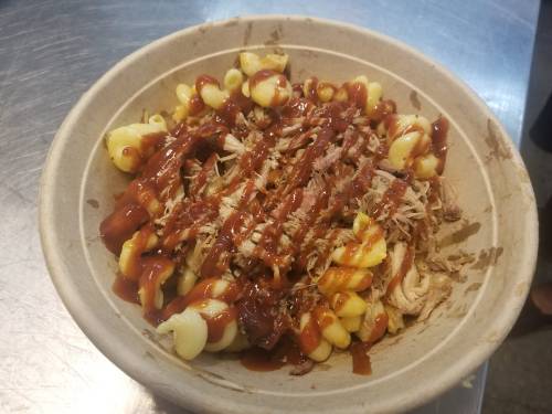 A bowl of pasta topped with shredded meat and drizzled with barbecue sauce.