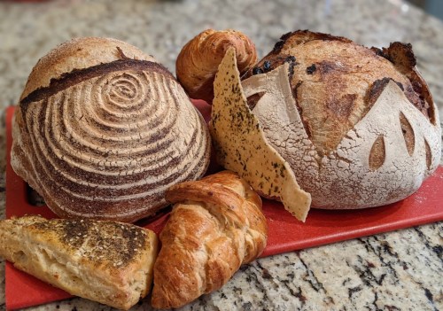 A variety of freshly baked breads, including round loaves, a croissant, and a flatbread, arranged on a red cutting board.