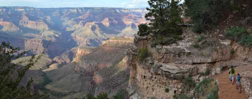 A scenic view of the Grand Canyon with hikers on a trail, showcasing layered rock formations and vast landscapes.