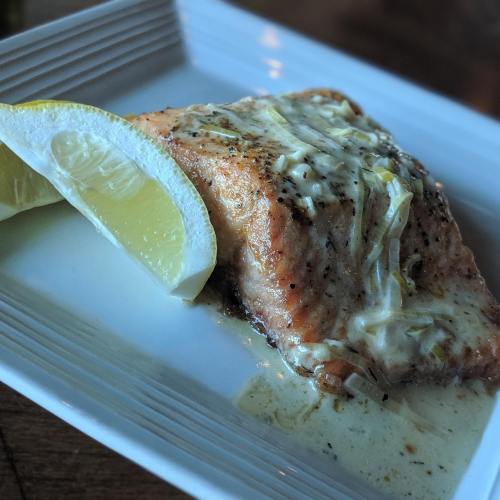 A piece of baked salmon topped with creamy sauce, served with a lemon wedge on a white plate.