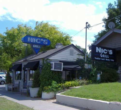 Exterior of Nic's Grill, featuring a blue sign, outdoor seating, and a welcoming atmosphere on a sunny day.
