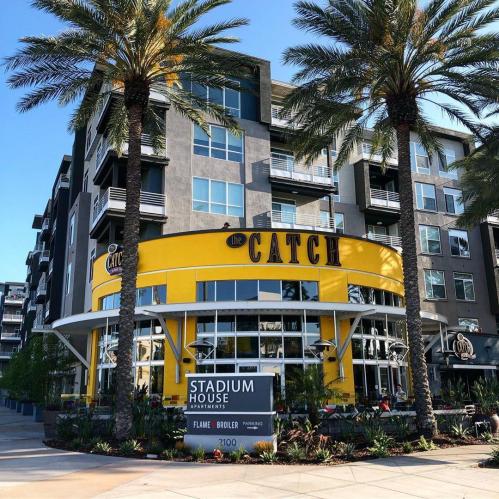 A modern apartment building with palm trees, featuring a bright yellow restaurant called "The Catch" at the entrance.
