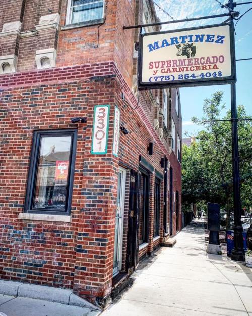 Exterior of Martinez Supermercado y Carnicería, a brick building with a sign, located on a sunny street corner.