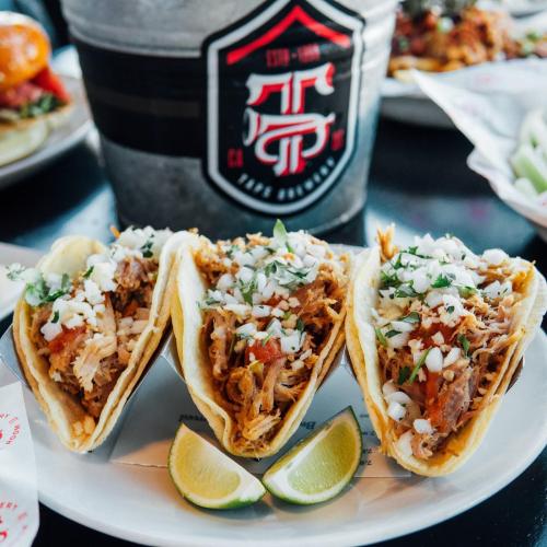 Three tacos filled with shredded meat, topped with onions and cilantro, served with lime wedges on a plate.