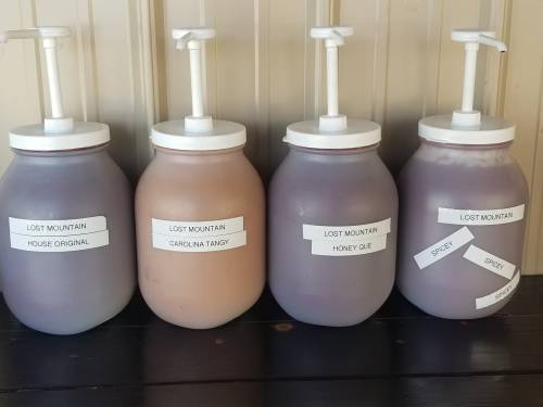 Four labeled jars with pumps, containing different sauces: House Original, Carolina Tangy, Honey Que, and Spicy.