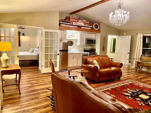 Cozy living area with leather sofas, a chandelier, and a kitchen, featuring warm wood tones and decorative accents.