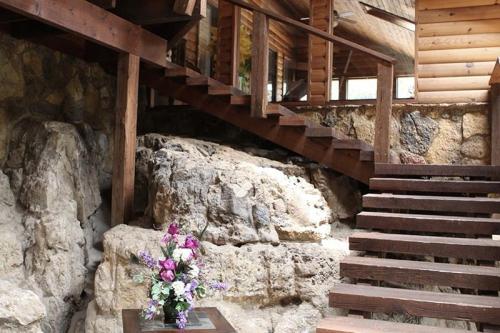 Interior of a rustic wooden building featuring a staircase and a small table with a vase of flowers on a rock surface.