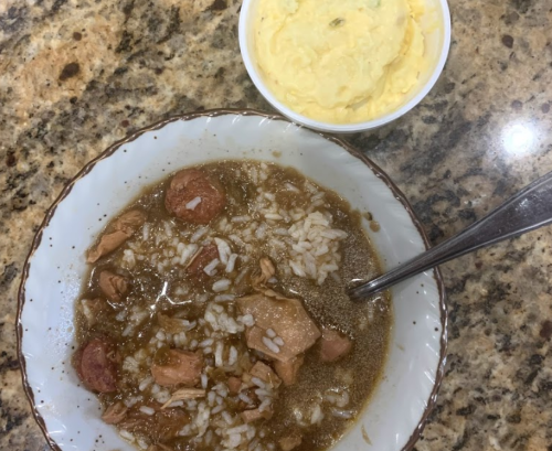 A bowl of rice with meat in a brown sauce, next to a small bowl of yellow mashed potatoes on a granite countertop.