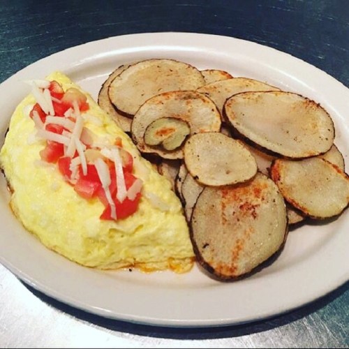 A plate featuring a fluffy omelette topped with tomatoes and cheese, accompanied by crispy potato slices.
