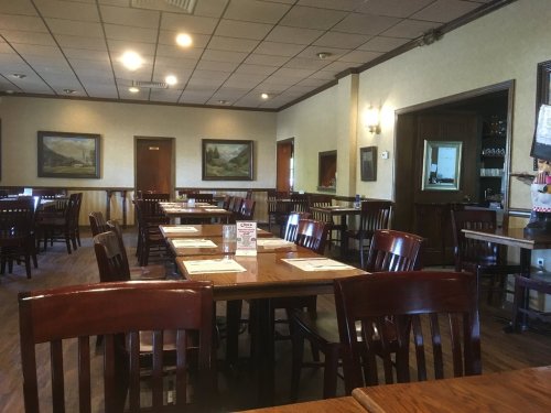Interior of a restaurant featuring wooden tables and chairs, with paintings on the walls and a warm, inviting atmosphere.