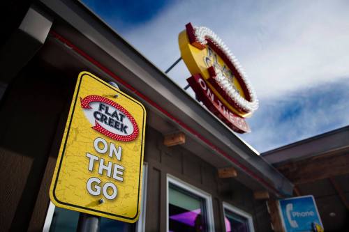 A yellow sign reading "Flat Creek On The Go" in front of a building with a colorful sign above.