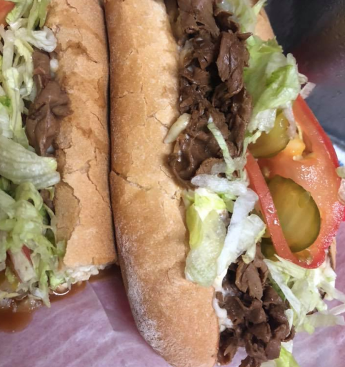 Two sandwiches filled with shredded beef, lettuce, tomatoes, and pickles, served in soft bread rolls.