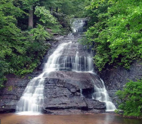 A serene waterfall cascading over rocky steps, surrounded by lush green trees and foliage.