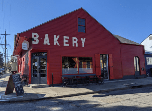 A bright red bakery building with large white letters, featuring outdoor seating and a clear blue sky.