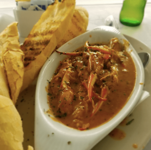 A dish of spicy seafood stew served with toasted bread, garnished with herbs and red chili peppers.