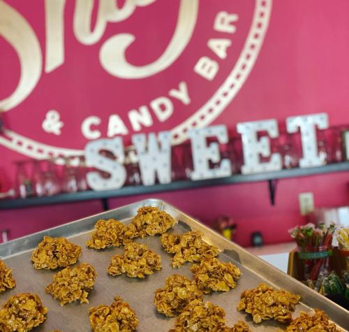 A tray of golden, crunchy treats in front of a vibrant pink wall with "SWEET" letters and a candy bar sign.