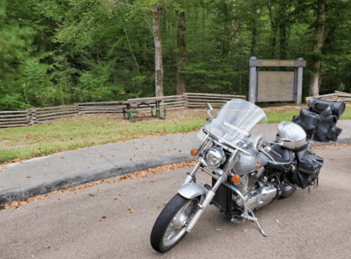 A silver motorcycle parked on a road near a wooded area and a sign for Guava Creek.
