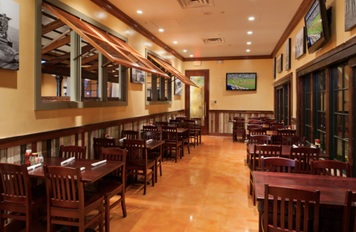 Interior of a restaurant featuring wooden tables, chairs, and large windows, with sports TVs on the walls.