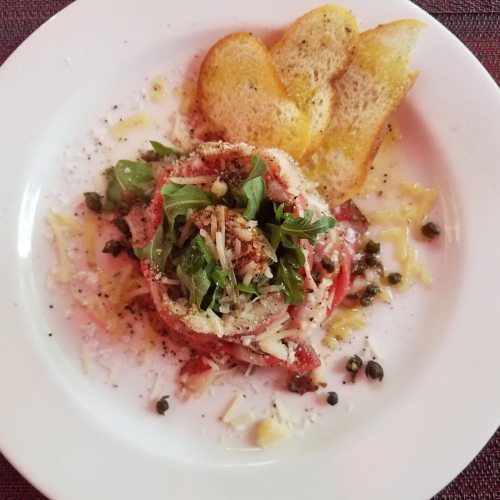 A plate of layered salad with greens, cheese, and capers, accompanied by toasted bread slices.