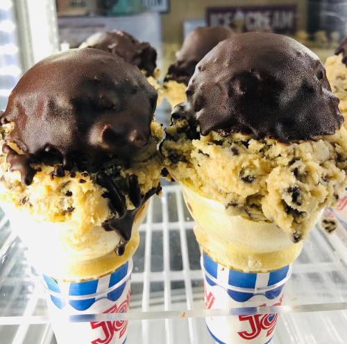 Two ice cream cones with chocolate-dipped scoops and cookie dough flavor, displayed in a freezer.