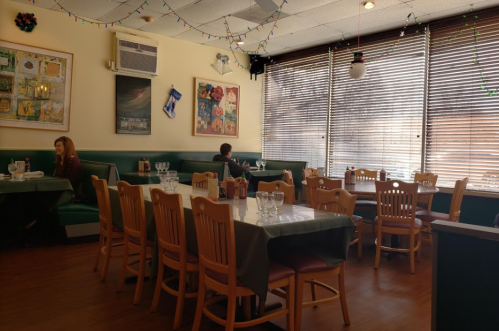 A cozy restaurant interior with green booths, wooden tables, and holiday decorations, featuring a few diners.
