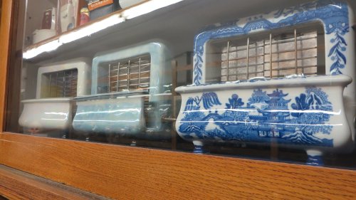 Three vintage toasters displayed behind glass, featuring intricate blue and white designs.