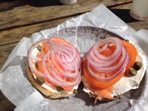 A bagel topped with cream cheese, smoked salmon, capers, and layered with sliced tomatoes and red onions.