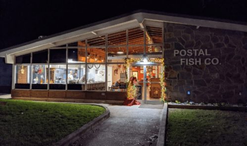 A festive building with "POSTAL FISH CO." sign, decorated for the holidays, featuring large windows and a welcoming entrance.