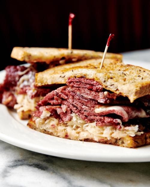 A close-up of a stacked sandwich with layers of pastrami and sauerkraut, held together with toothpicks.