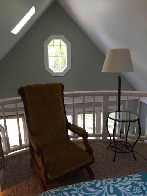 Cozy attic space featuring a vintage rocking chair, a lamp, and a small side table by a window.