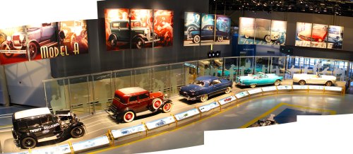 A display of vintage cars in a museum, featuring various models and colorful wall art in the background.