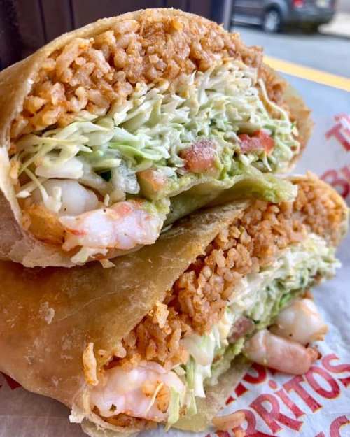 A close-up of a burrito filled with shrimp, rice, lettuce, and guacamole, wrapped in a tortilla.