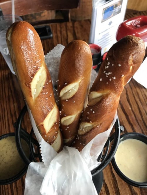 Three soft pretzels in a basket, sprinkled with salt, served with two dipping sauces.