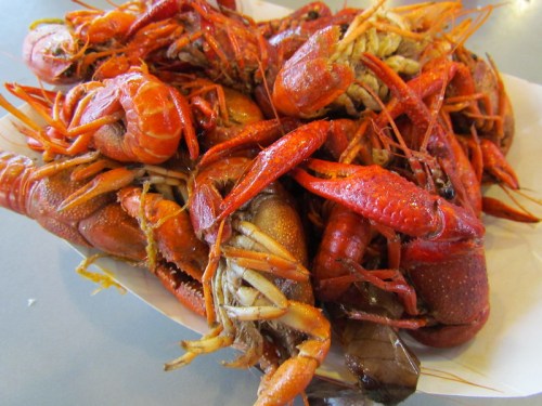 A close-up of a pile of cooked, red crawfish on a white paper plate.