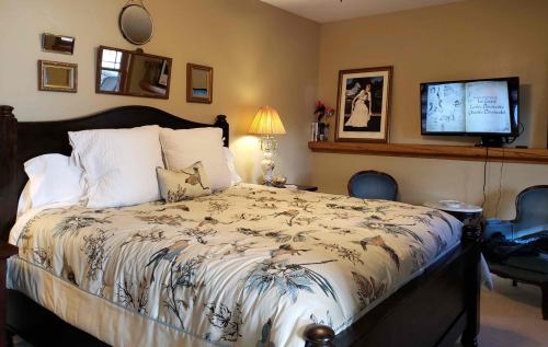 Cozy bedroom with a floral bedspread, decorative mirrors, a lamp, and a TV on the wall.
