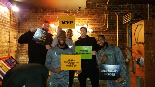 A group of six people holding signs with phrases like "MVP," "Mission Accomplished," and "Legendary Heroes" in a cozy setting.