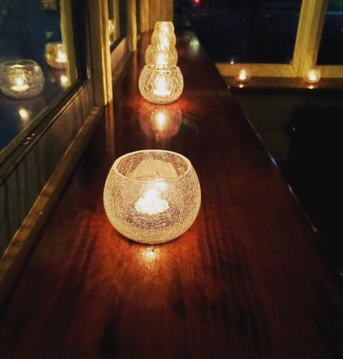 A row of glowing candle holders on a wooden surface, casting warm light in a cozy setting.