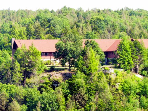 A lodge nestled among lush green trees on a hillside, surrounded by dense forest.