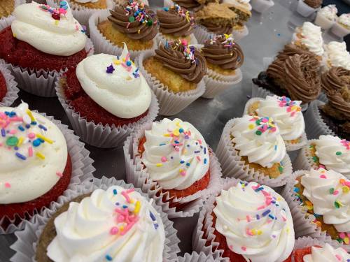 A variety of colorful cupcakes with frosting and sprinkles, arranged on a table.