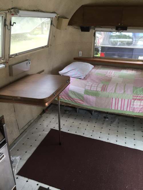 Interior of a vintage camper with a bed, small table, and kitchenette area, featuring a cozy, simple design.