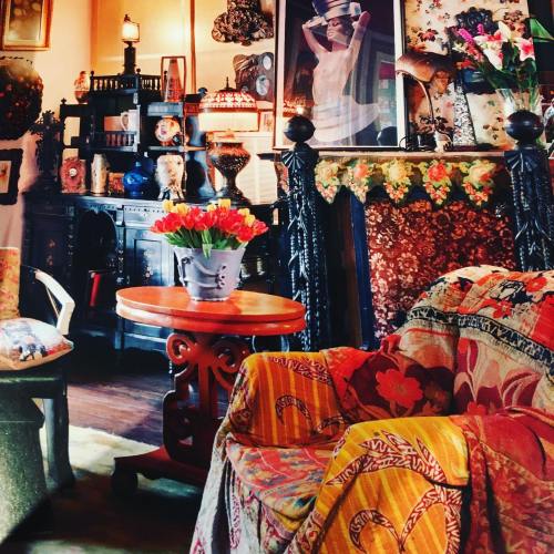 Cozy vintage living room with colorful decor, a floral arrangement, and an ornate fireplace adorned with art.