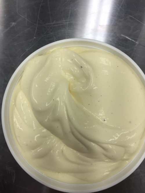 A close-up of creamy, smooth vanilla custard in a white container, with a shiny surface and swirls.