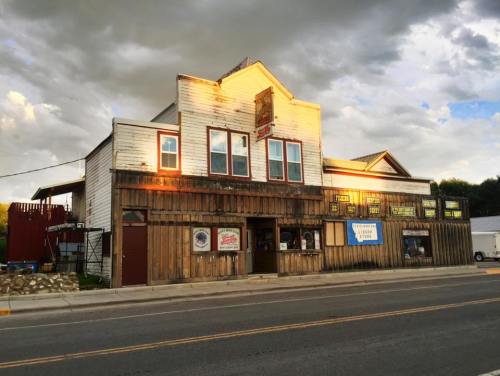A rustic wooden building with large windows, featuring a sign and various storefronts, under a cloudy sky.