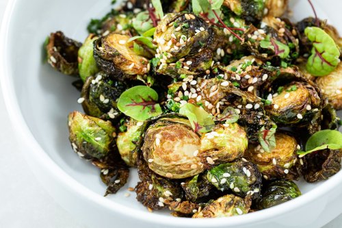 A bowl of roasted Brussels sprouts topped with sesame seeds and microgreens.