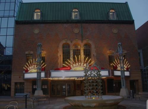 Historic theater facade with bright marquee lights and a decorative fountain in front, set against a twilight sky.